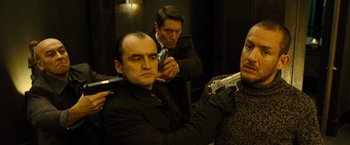 Movie still from “Micmacs” (2009), directed by Jean-Pierre Jeunet – A group of men holding guns in front of a mirror; Medium shot, Low angle