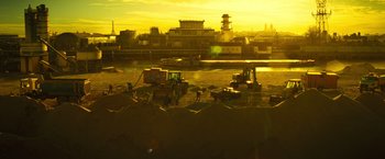 Movie still from “Micmacs” (2009), directed by Jean-Pierre Jeunet – A view of a city at sunset from a beach; Extreme Wide shot, High angle