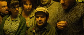Movie still from “Micmacs” (2009), directed by Jean-Pierre Jeunet – A group of people standing next to each other in a room; Medium shot, High angle