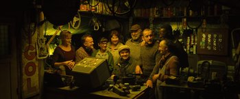 Movie still from “Micmacs” (2009), directed by Jean-Pierre Jeunet – A group of people standing around a table; Wide shot, High angle