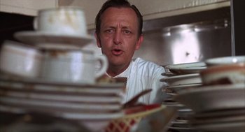 Movie still from “Midnight Cowboy” (1969), directed by John Schlesinger – A man in white shirt and neck tie looking at plates; Close Up shot, Low angle