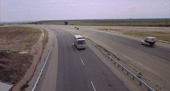 Movie still from “Midnight Cowboy” (1969), directed by John Schlesinger – A bus driving down a road near a field; Extreme Wide shot, High angle