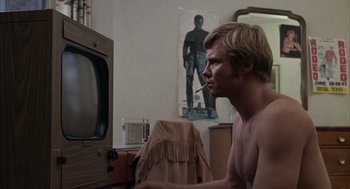 Movie still from “Midnight Cowboy” (1969), directed by John Schlesinger – A man smoking a cigarette in front of a television; Medium shot, Over the shoulder angle