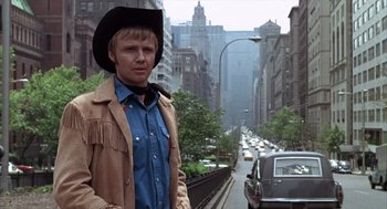 Movie still from “Midnight Cowboy” (1969), directed by John Schlesinger – A man wearing a cowboy hat standing on the side of the road; Medium shot, Low angle