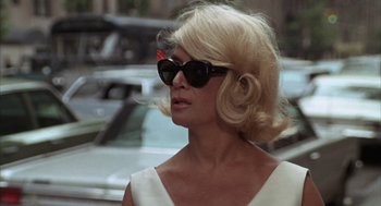 Movie still from “Midnight Cowboy” (1969), directed by John Schlesinger – A woman with blonde hair wearing sunglasses and a white dress; Close Up shot, Over the shoulder angle