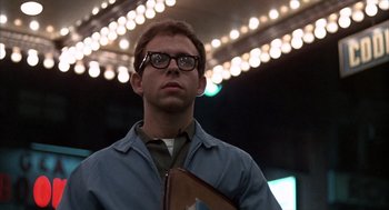 Movie still from “Midnight Cowboy” (1969), directed by John Schlesinger – A man with glasses is holding a book; Medium shot, Low angle
