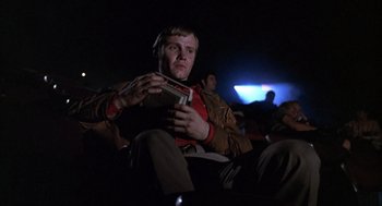 Movie still from “Midnight Cowboy” (1969), directed by John Schlesinger – A man sitting in a dark room holding a nintendo wii game controller; Medium shot, Low angle