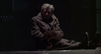 Movie still from “Midnight Cowboy” (1969), directed by John Schlesinger – An old man sitting on the ground wearing a coat and mittens; Medium shot, High angle