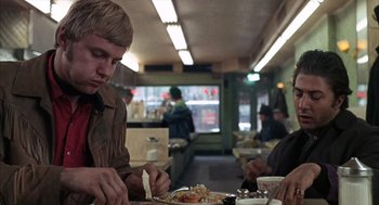 Movie still from “Midnight Cowboy” (1969), directed by John Schlesinger – A man sitting at a table with a plate of food in front of him; Medium shot, Over the shoulder angle