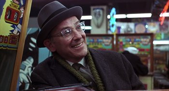 Movie still from “Midnight Cowboy” (1969), directed by John Schlesinger – An older man wearing a hat and glasses smiling; Close Up shot, Over the shoulder angle