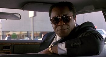 Movie still from “Midnight Run” (1988), directed by Martin Brest – A man sitting in the back seat of a car wearing sunglasses; Close Up shot, Low angle