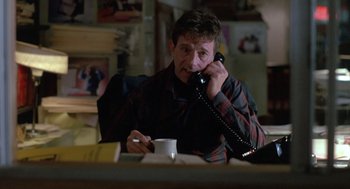 Movie still from “Midnight Run” (1988), directed by Martin Brest – A man sitting at a table talking on the phone; Medium shot, Low angle