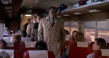 Movie still from “Midnight Run” (1988), directed by Martin Brest – A man in a trench coat walking on a train; Medium shot, Over the shoulder angle