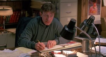 Movie still from “Midnight Run” (1988), directed by Martin Brest – A man sitting at a desk writing on a notebook; Medium shot, High angle