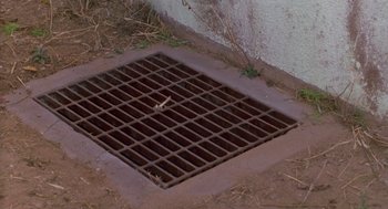 Movie still from “Midnight Run” (1988), directed by Martin Brest – A grate in the middle of the ground near a wall; Extreme Close Up shot, Overhead angle