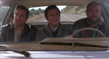 Movie still from “Midnight Run” (1988), directed by Martin Brest – A man sitting in the back seat of a car; Medium shot, High angle