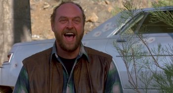 Movie still from “Midnight Run” (1988), directed by Martin Brest – A man with a goatee and a leather jacket is smiling; Medium shot, Low angle