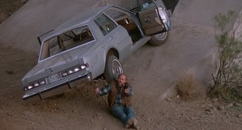 Movie still from “Midnight Run” (1988), directed by Martin Brest – A man sitting on the ground next to an old car; Wide shot, High angle