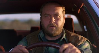 Movie still from “Midnight Run” (1988), directed by Martin Brest – A man with a beard is driving a car; Close Up shot, Low angle