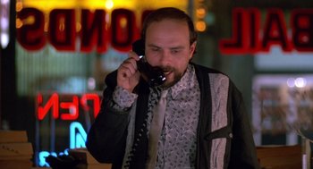 Movie still from “Midnight Run” (1988), directed by Martin Brest – A man talking on a phone while standing in front of a neon sign; Medium shot, Low angle