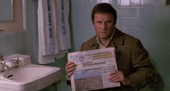 Movie still from “Midnight Run” (1988), directed by Martin Brest – A man holding a newspaper in a bathroom; Close Up shot, Over the shoulder angle