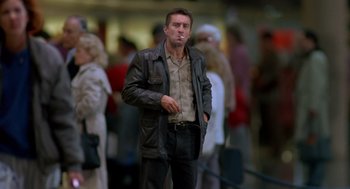 Movie still from “Midnight Run” (1988), directed by Martin Brest – A man smoking a cigarette while standing in a crowd of onlookers; Medium shot, Low angle