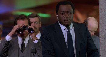 Movie still from “Midnight Run” (1988), directed by Martin Brest – A man in a suit and tie holding a camera and taking a picture; Close Up shot, Over the shoulder angle