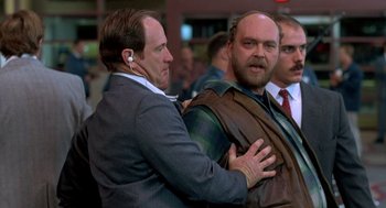 Movie still from “Midnight Run” (1988), directed by Martin Brest – Two men in suits and one has his hands on the shoulder of another man; Medium shot, Over the shoulder angle