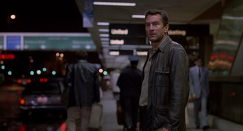 Movie still from “Midnight Run” (1988), directed by Martin Brest – A man in a leather jacket standing next to luggage; Medium shot, Low angle