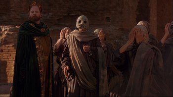 Movie still from “Mighty Aphrodite” (1995), directed by Woody Allen – A group of people wearing masks in a cave; Medium shot, Low angle