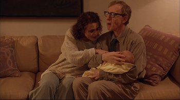 Movie still from “Mighty Aphrodite” (1995), directed by Woody Allen – An older man and woman holding a baby on a couch; Medium shot, High angle