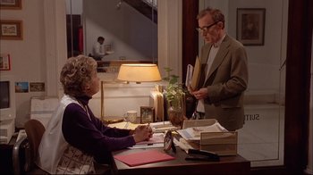 Movie still from “Mighty Aphrodite” (1995), directed by Woody Allen – An older man and a woman at a desk; Medium shot, Over the shoulder angle