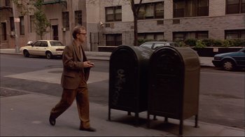 Movie still from “Mighty Aphrodite” (1995), directed by Woody Allen – A man walking down a street past two mailboxes; Wide shot, Low angle
