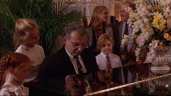 Movie still from “Mighty Aphrodite” (1995), directed by Woody Allen – A group of people standing next to each other at a piano; Medium shot, High angle