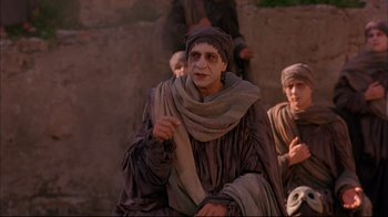 Movie still from “Mighty Aphrodite” (1995), directed by Woody Allen – A man dressed as an old man sitting next to a wall; Medium shot, Over the shoulder angle