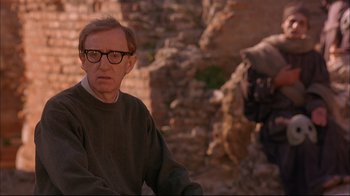 Movie still from “Mighty Aphrodite” (1995), directed by Woody Allen – A man wearing glasses is standing in front of a brick wall; Medium shot, Over the shoulder angle