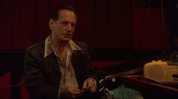 Movie still from “Mighty Aphrodite” (1995), directed by Woody Allen – A man sitting in front of a piano holding a cell phone; Medium shot, Low angle