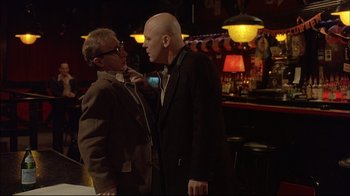 Movie still from “Mighty Aphrodite” (1995), directed by Woody Allen – A man in a suit and a man in a tie in front of a bar; Medium shot, Low angle