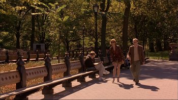 Movie still from “Mighty Aphrodite” (1995), directed by Woody Allen – A couple of people walking down a sidewalk near a park bench; Wide shot, Over the shoulder angle