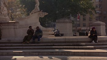 Movie still from “Mighty Aphrodite” (1995), directed by Woody Allen – A group of people sitting on steps in front of a statue; Wide shot, High angle