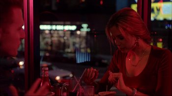 Movie still from “Mighty Aphrodite” (1995), directed by Woody Allen – A woman sitting at a table in front of drinks; Medium shot, Over the shoulder angle