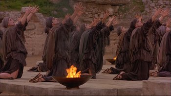 Movie still from “Mighty Aphrodite” (1995), directed by Woody Allen – A group of men in robes kneeling down in front of a fire pit; Wide shot, Low angle
