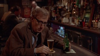 Movie still from “Mighty Aphrodite” (1995), directed by Woody Allen – A man sitting at a table with a glass of beer in front of him; Medium shot, Over the shoulder angle