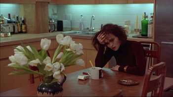 Movie still from “Mighty Aphrodite” (1995), directed by Woody Allen – A woman sitting at a table with a cup of coffee; Medium shot, High angle