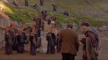 Movie still from “Mighty Aphrodite” (1995), directed by Woody Allen – A group of people standing in front of a stone wall; Extreme Wide shot, High angle