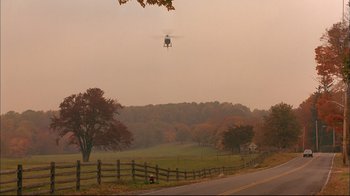 Movie still from “Mighty Aphrodite” (1995), directed by Woody Allen – A helicopter flying low over a field near a road; Extreme Wide shot, High angle
