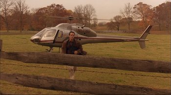 Movie still from “Mighty Aphrodite” (1995), directed by Woody Allen – A man sitting in front of a helicopter in a field; Wide shot, High angle