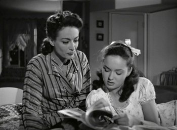 Movie still from “Mildred Pierce” (1945), directed by Michael Curtiz – Two women are looking at a magazine in a kitchen; Medium shot, High angle