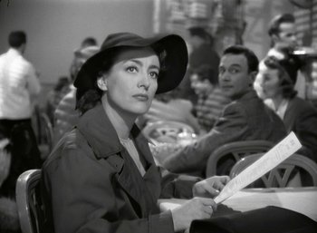 Movie still from “Mildred Pierce” (1945), directed by Michael Curtiz – A woman sitting at a table in front of other people; Medium shot, Over the shoulder angle