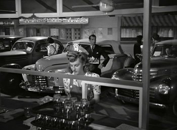 Movie still from “Mildred Pierce” (1945), directed by Michael Curtiz – An old photo of a woman sitting in front of a car; Wide shot, High angle